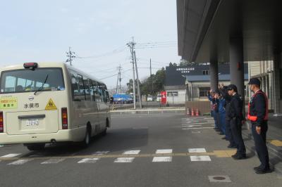 小学生がバスで帰るのを見送る警察官の写真